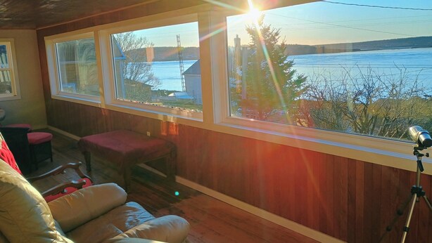 Ein Zimmer mit Holzboden, einer Ledersofa, einer roten Bank und einem Fenster mit Blick auf ein Gewässer.