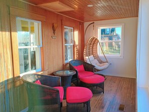 A wooden-paneled room with wicker furniture, a hanging chair, and a small table.