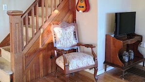 Eine Holztreppe, ein mit Blumenmuster versehener Stuhl, eine Gitarre und ein Fernseher auf einem Holzgestell.