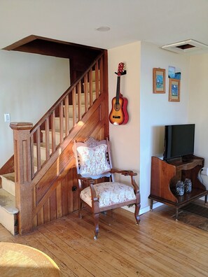 Un escalier en bois, une chaise à motifs floraux, une guitare et un téléviseur posé sur un meuble en bois.