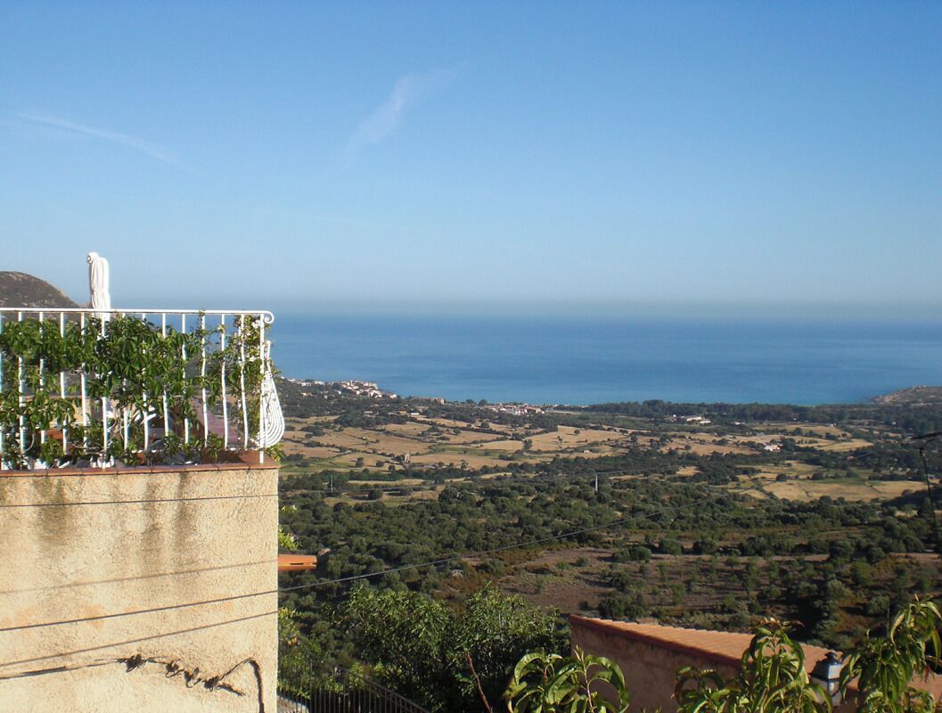 A coastal view with a building featuring a balcony with plants and a white object on it.