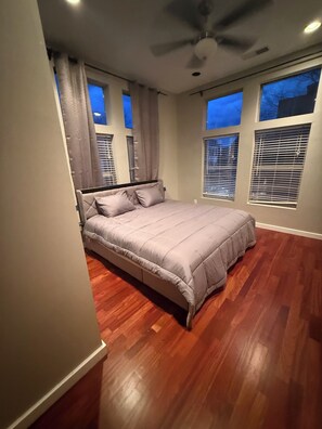 Ein Schlafzimmer mit einem Bett, Deckenventilator und großen Fenstern.