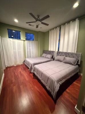 Ein Schlafzimmer mit zwei Betten, einem Deckenventilator und einem Fenster mit Vorhängen.