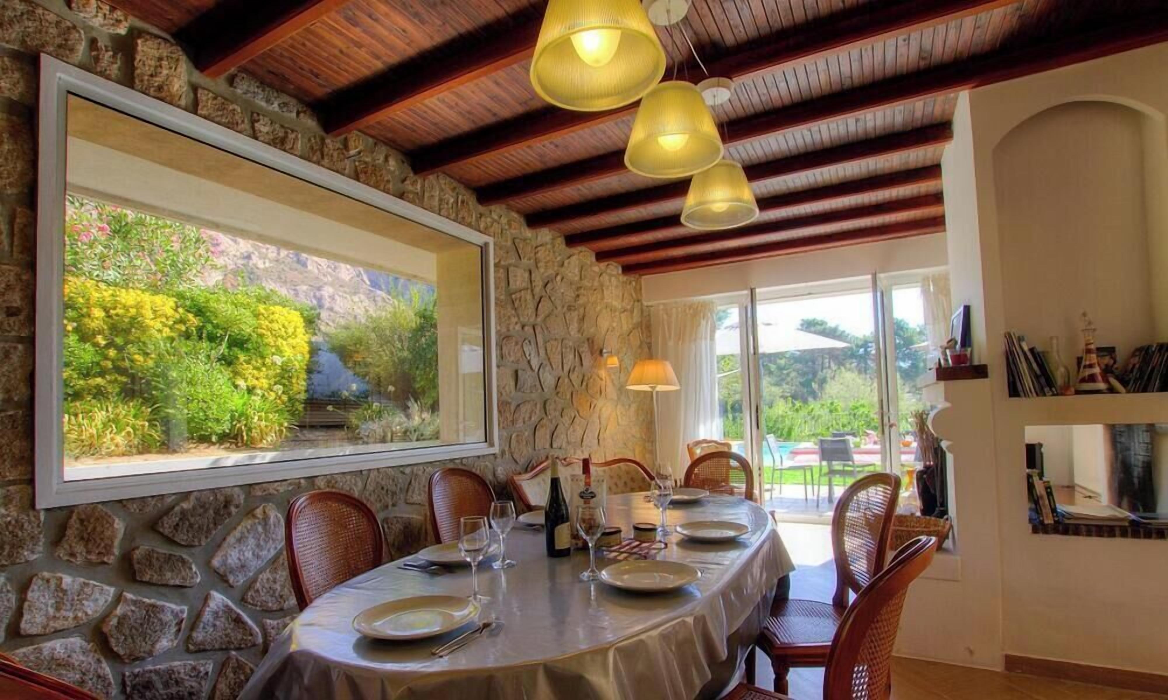 A dining area with a stone wall, wooden ceiling beams, and a table set for four.