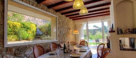 A dining area with a stone wall, wooden ceiling beams, and a table set for four.