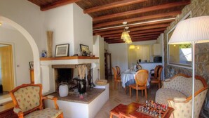 A cozy living room with a fireplace, wooden beams, and a dining area with chairs and a table. - The villa - AFA - Gîte (AFA)