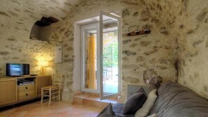 A stone-walled room with a television, a wooden cabinet, a sofa, and a sliding glass door leading outside. - Domaine Vecchio 2 - CHIATRA DI VERDE (CHIATRA DI VERDE)