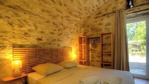 A bedroom with a stone wall, wooden headboard, bedside lamps, a bed with pillows, a wooden shelf, and a window with curtains. - Domaine Vecchio 2 - CHIATRA DI VERDE (CHIATRA DI VERDE)