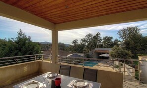 Ein Balkon mit Esstisch, der einen Pool und eine gebirgige Landschaft blickt.