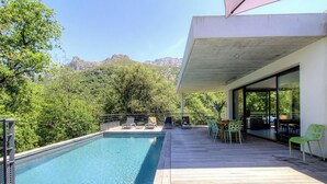 Una piscina con lettini e un tavolo su un pontile di legno, con vista su un paesaggio montuoso.