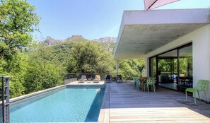Ein Swimmingpool mit Liegestühlen und einem Tisch auf einer Holzterrasse, mit Blick auf eine Berglandschaft.