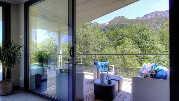 Un balcone con una porta vetrata, mobili da esterno e vista su un paesaggio montano.