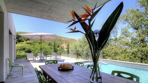 Un patio esterno con tavolo e sedie in legno, un vaso con fiori e una piscina.