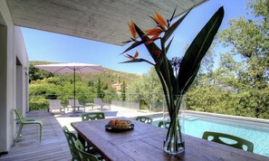 Eine Terrasse im Freien mit einem Holztisch, Stühlen, einer Vase mit Blumen und einem Pool.