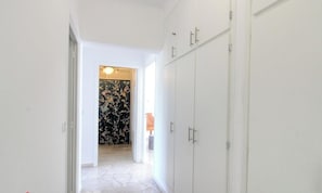 Ein Korridor mit weißen Wänden, Holzboden und einer Tür zu einem Zimmer mit floralem Wandpapier.