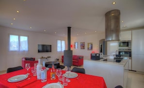 Una cucina moderna con forno e microonde integrati, un'area pranzo con tavolo rosso apparecchiata per quattro persone e un soggiorno con divano rosso e TV a parete.