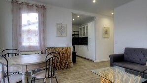 Ein Wohnzimmer mit Esstisch, Stühlen, einer Couch und einer Küche im Hintergrund.