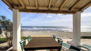 Taula i cadires de fusta sota una pergola de fusta, amb vista a la platja i l'oceà.