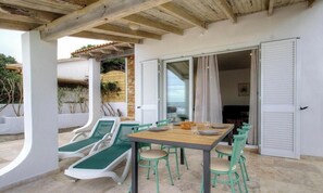 An outdoor patio with a table and chairs, a covered area with a wooden ceiling, and a sliding glass door leading to an interior space. - Quenza, N°18 - GHISONACCIA (GHISONACCIA)