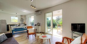 Ein modernes Wohnzimmer mit Sofa, Sesseln, einem kleinen Tisch, einem Fernseher und einer Küche im Hintergrund.