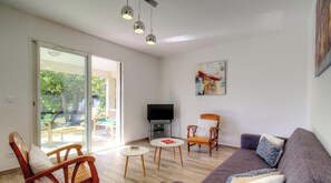 Ein Wohnzimmer mit einer Couch, einem Sessel, einem kleinen Tisch, einem Fernseher und einem Bild an der Wand.