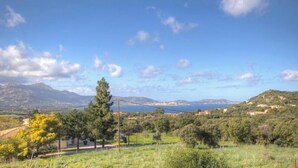 Paesaggio costiero con cielo sereno, montagne in lontananza e un tratto d'acqua.