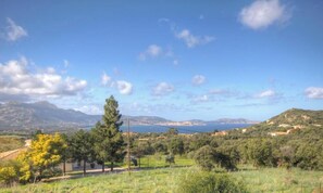 Eine Küstenlandschaft mit blauem Himmel, fernen Bergen und einem Gewässer.