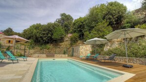Ein Swimmingpool mit Liegestühlen und Sonnenschirmen, umgeben von Steinmauern und viel Grün.