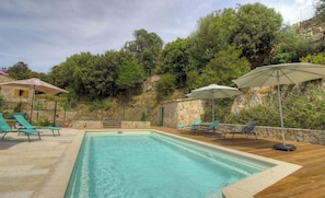 Ein Swimmingpool mit Liegestühlen und Sonnenschirmen, umgeben von Steinmauern und viel Grün.