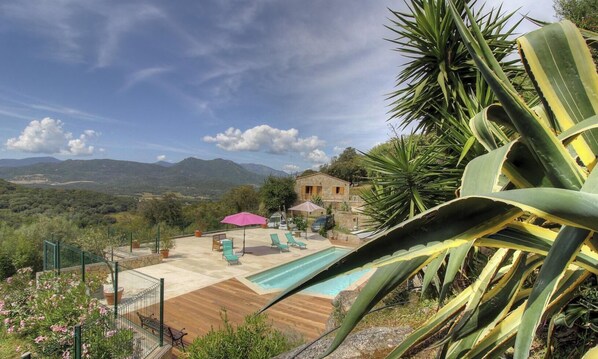 Ein Pool mit Liegestühlen, eine Terrasse und Blick auf Berge.