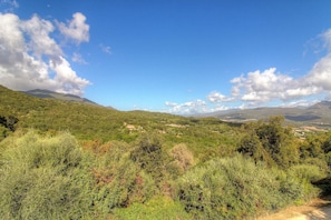 Eine gebirgige Landschaft mit vereinzelten Gebäuden und blauem Himmel.