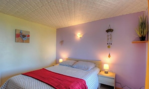 Ein Schlafzimmer mit einem Bett, zwei Nachttischlampen, einer Wandleuchte, einer hängenden Pflanze und einem Gemälde.