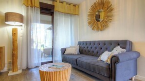 A living room with a grey sofa, a round wooden coffee table, a floor lamp, and a sunburst mirror on the wall. - Résidence U Quarciu - GHISONACCIA (GHISONACCIA)