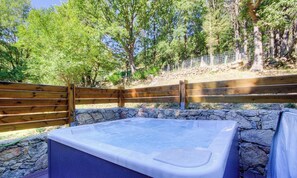 Ein Whirlpool, umgeben von einer Steinmauer und einem Holzzaun, mit Bäumen im Hintergrund.