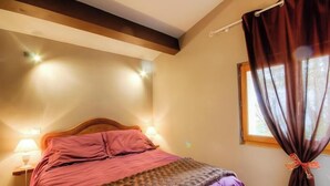 Quarto com cabeceira de madeira, cama com roupa de cama rosa, duas luminárias de apoio e uma janela com cortinas.