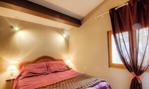 Ein Schlafzimmer mit einem hölzernen Kopfende, einem Bett mit pinkener Bettwäsche, zwei Nachttischlampen und einem Fenster mit Vorhängen.