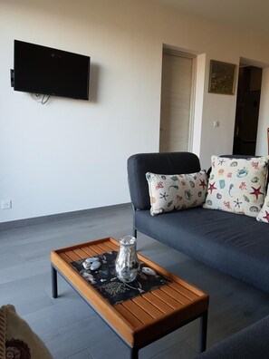 Ein Wohnzimmer mit einer Couch, einem flachbildfernseher an der Wand, einem Couchtisch aus Holz und dekorativen Gegenständen sowie gemusterten Kissen.