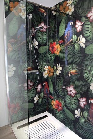 Eine Dusche mit Glastür und tropisch-floralem Fliesendesign.