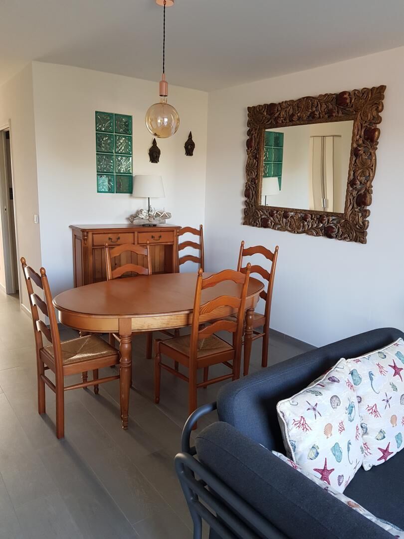 Een eethoek met een houten tafel en stoelen, een hanglamp, een decoratieve spiegel en een bank met een gekleurd kussen.