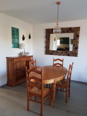 Ein Essbereich mit einem Holztisch und Stühlen, einem Schrank, einem Spiegel mit aufwendiger Rahmenverzierung und einer Pendelleuchte.