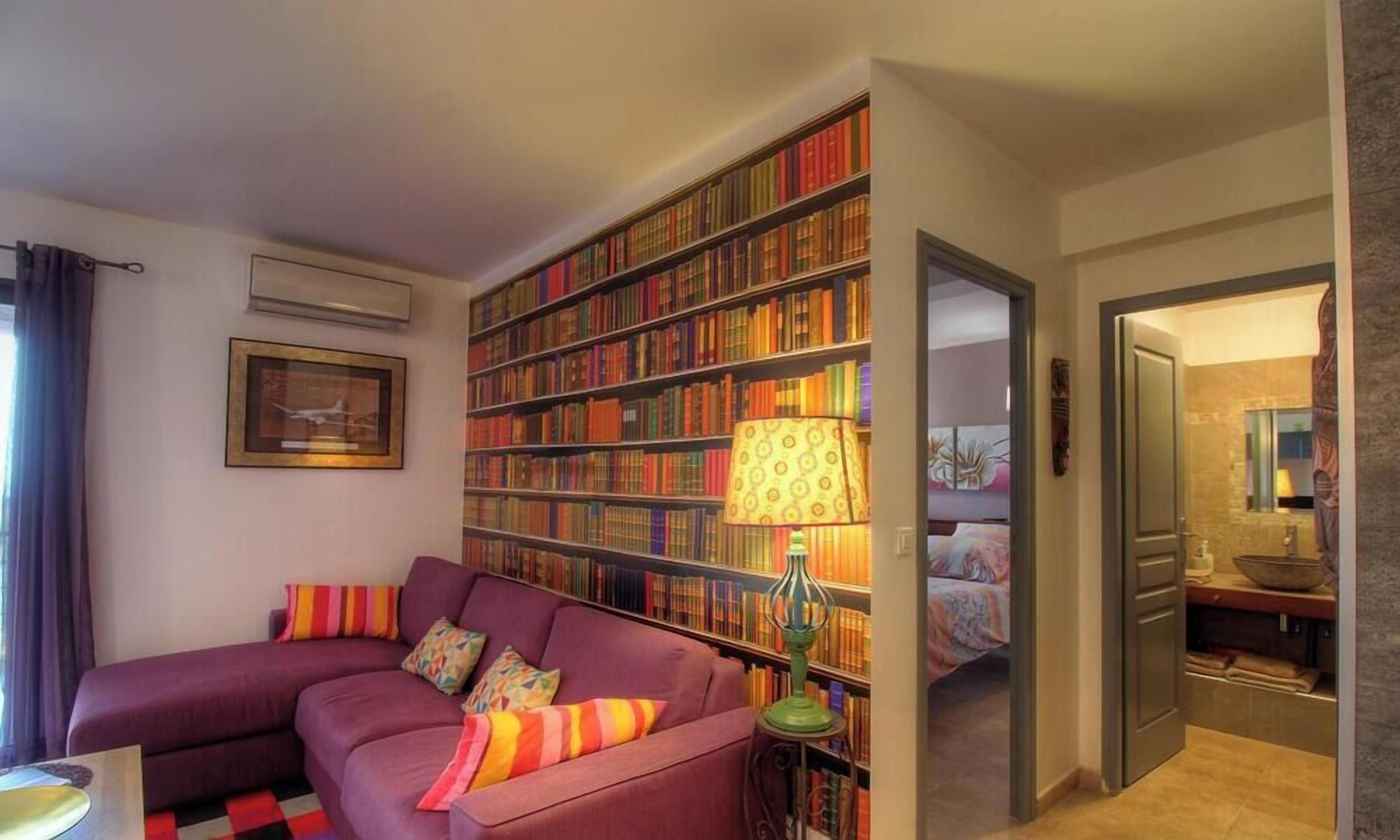 Un salon avec un canapé violet, une bibliothèque et une lampe.
