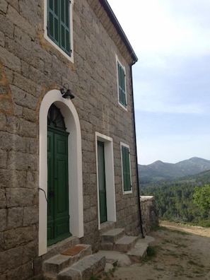 Ein Steinhaus mit einer grünen Tür und Fenstern, einer Steintreppe und einer bergigen Kulisse.
