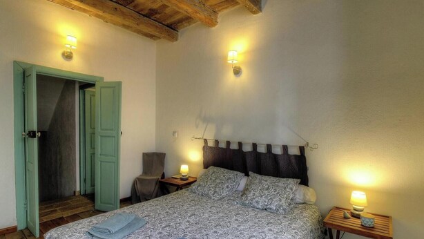 Ein Schlafzimmer mit einem Bett, zwei Nachttischen mit Lampen, einem Sessel und einer offenen Tür zu einem anderen Raum.