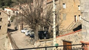 Un poble de muntanya amb cases de pedra, un carrer pavimentat i cotxes estacionats.