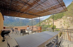 Una terraza con vistas a montañas y un pueblo, amueblada con mesas y sillas.