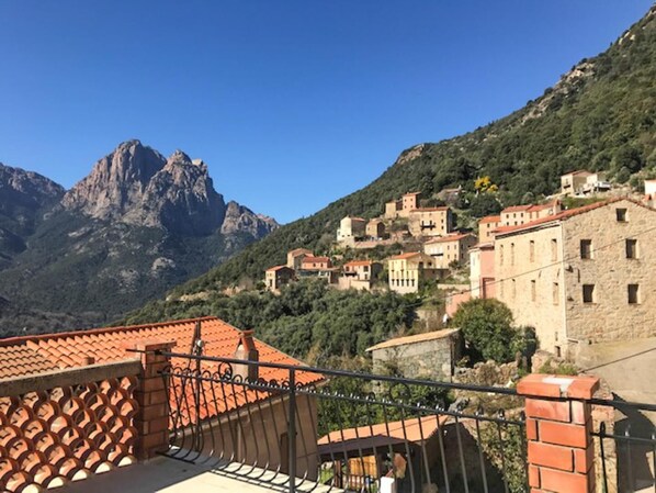 A mountainous village with terracotta-roofed buildings, a prominent rocky peak in the background, and a balcony with a wrought-iron railing. - I Monti Signori - OTA (OTA)