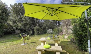 Een terras met tafels, stoelen, een gele parasol en een stenen bank.