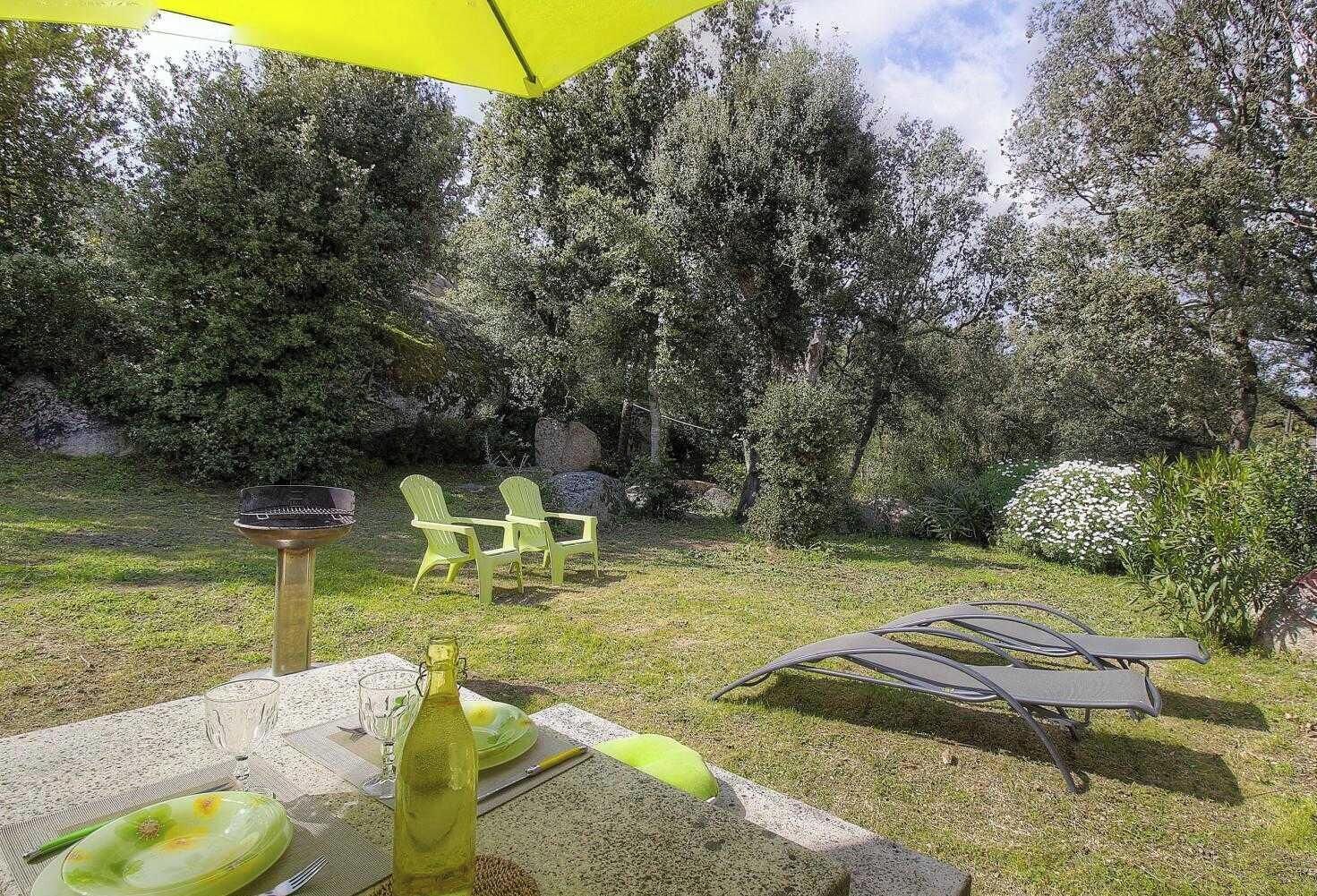 An outdoor patio with a table set for dining, two green chairs, a yellow umbrella, and a grill.