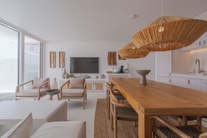 Un salon moderne avec une table à manger en bois, des sièges confortables, un grand téléviseur à écran plat et un luminaire original en fibres tressées.