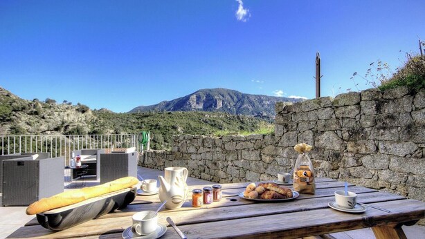 Tavolo di legno apparecchiato per un picnic, con cibo e bevande, con vista su un paesaggio montuoso.
